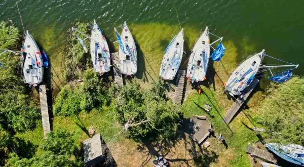 Mazury atrakcje wodne: białe żaglówki cumują przy brzegu, zielona trawa i drzewa tworzą malowniczy krajobraz.
