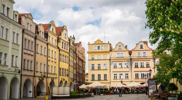 Kolorowe kamienice na jeleniogórskim rynku, z arkadami i kawiarnianymi ogródkami, pod błękitnym niebem.