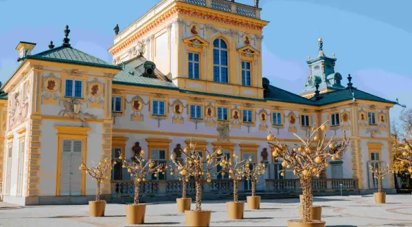 Barokowy pałac, jeden z pięknych muzeów w Polsce, z ozdobnymi drzewkami w donicach przed fasadą.