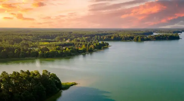 Zachód słońca nad jeziorem, z lasem i domkami w tle. Idealne, fajne miejsca nad jeziorem na relaks.
