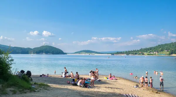 Polańczyk atrakcje: plażowicze odpoczywają nad Soliną, w tle żaglówka i zielone wzgórza.