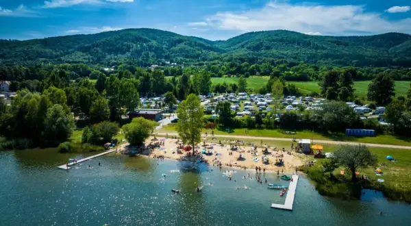 Letnie słońce nad jeziorem Bielawskim. Tłumy plażowiczów, kemping i zielone wzgórza w tle.