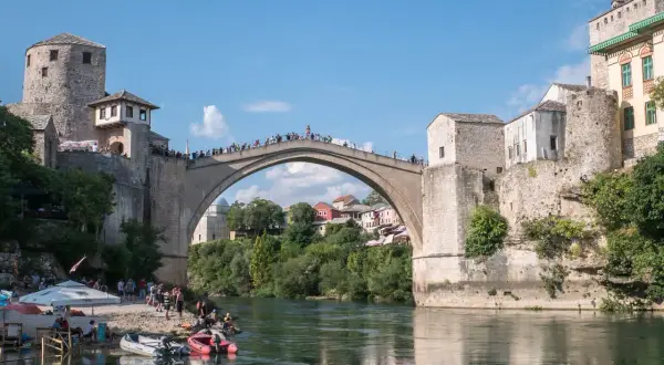 Mostar, Bośnia i Hercegowina: Słynny Stary Most z kamienia, tłumy ludzi na moście i brzegu, łodzie na rzece Neretwie.