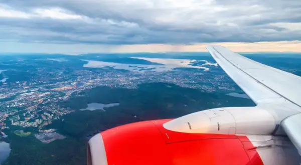 Widok z samolotu na Oslo Torp i okoliczne fiordy. Czerwony silnik i białe skrzydło samolotu na pierwszym planie.