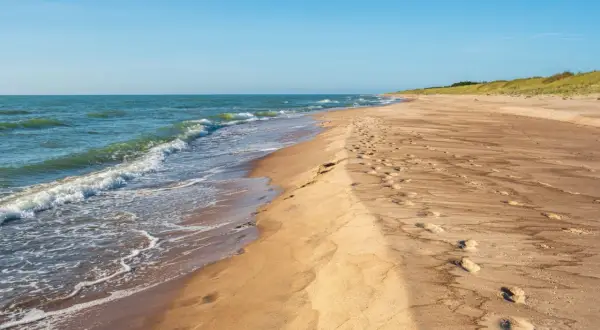 Spokojne, dzikie plaże nad Bałtykiem. Fale delikatnie obmywają piaszczysty brzeg, a na piasku widać ślady stóp.