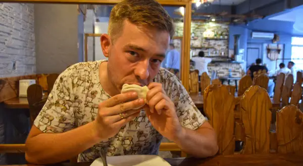 Mężczyzna je pierożki, delektując się smakami kuchni gruzińskiej w przytulnej restauracji.