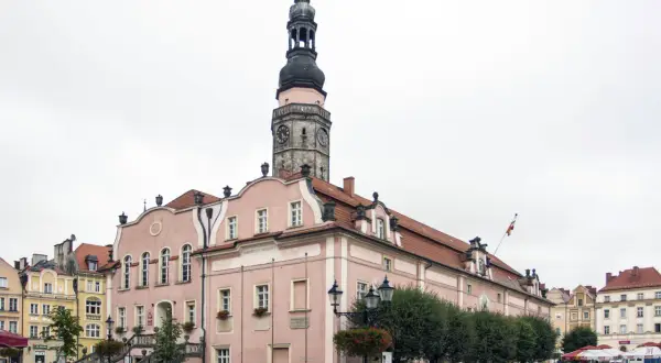 Różowy ratusz z wieżą zegarową to główna z bolesławiec atrakcje. Na rynku widać też kamienice i kawiarniane stoliki.