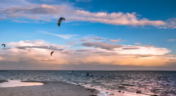 Zachód słońca nad Bałtykiem. Kilku śmiałków uprawia kitesurfing w Polsce, unosząc się na falach pod kolorowym niebem.