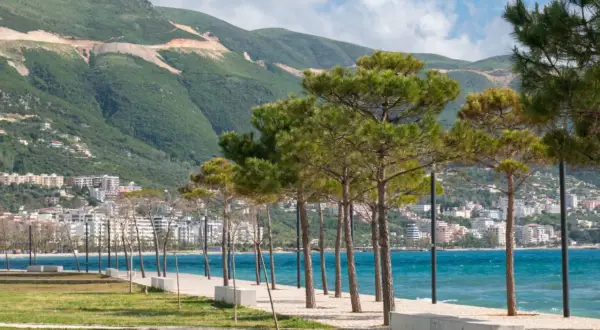 Wlora, Albania: nadmorska promenada z sosnami, turkusowe morze i góry w tle.