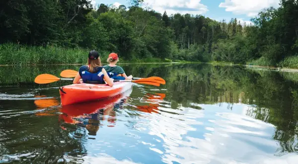 Dwie osoby płyną kajakiem po spokojnej rzece, ciesząc się pięknem przyrody. To idealny spływ kajakowy Mazury.