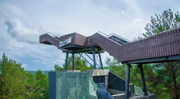 Drewniana konstrukcja widokowa na górze Markowca w Rumi, z widocznymi schodami i balustradami, otoczona zielenią drzew.