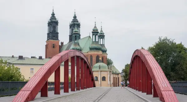 Czerwony most na poznańskiej trasie prowadzi do katedry. Spacerowicze podziwiają architekturę.