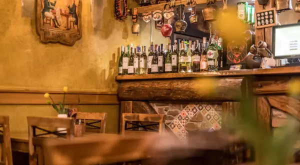 Drewniane stoły i krzesła w przytulnych restauracjach w Szklarskiej Porębie. Na półce rząd butelek wina, a nad nimi ozdoby.