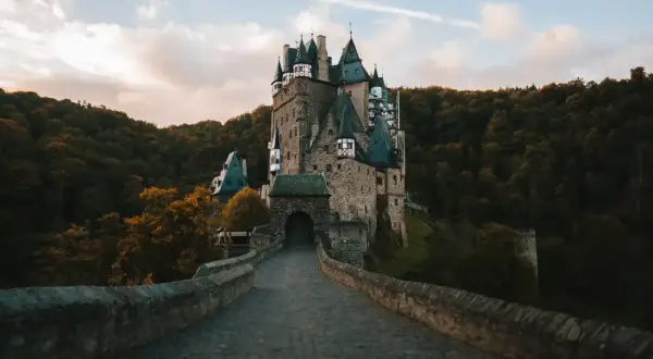 Zamek Eltz, jedna z najpiękniejszych atrakcji Niemiec, otoczony jesiennym lasem. Kamienny most prowadzi do bramy.
