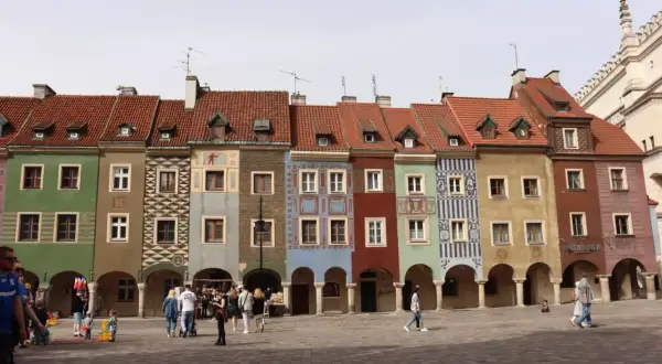 Kolorowe kamieniczki na poznańskim rynku, z arkadami i ludźmi spacerującymi po bruku.
