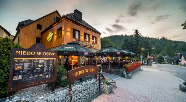 Restauracja "Niebo w Gębie" w Karpaczu oferuje pyszne jedzenie. Widać tu menu i stoliki na zewnątrz.