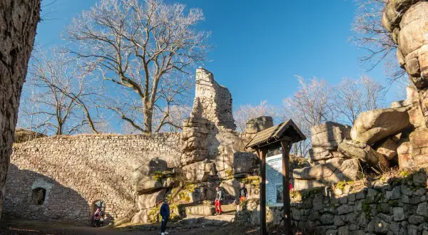 Ruiny zamku na Rudawach Janowickich, kamienne mury, skalne formacje i nagie drzewa pod błękitnym niebem.