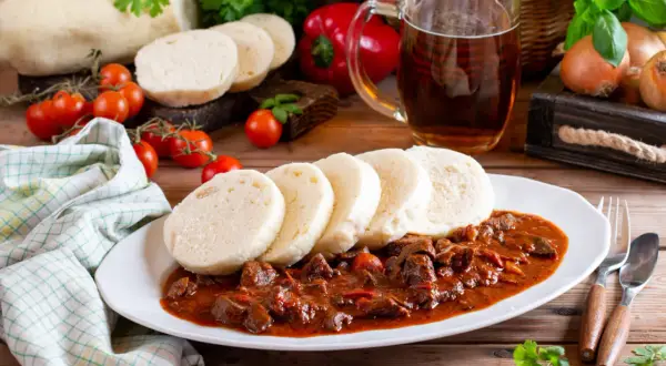 Gulasz z knedlikami, klasyka kuchni czeskiej, podany z piwem i świeżymi warzywami.