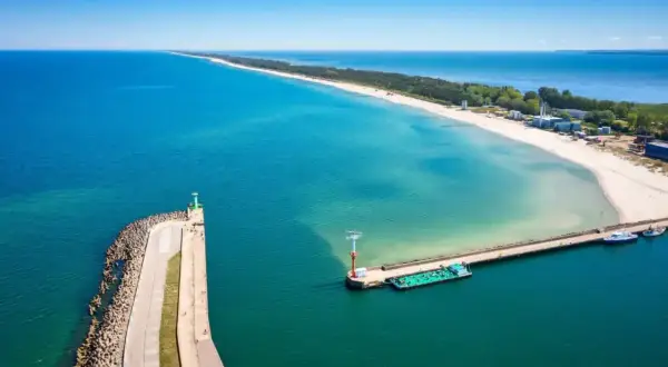 Molo we Władysławowie, z falochronem i latarnią morską, wita statki na tle piaszczystej plaży i turkusowego morza.