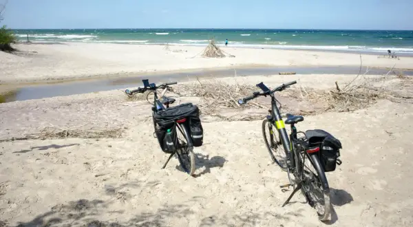 Dwa rowery z sakwami na piaszczystej plaży, gotowe na odkrywanie tras rowerowych nad morzem. W tle widać morze i niebo.