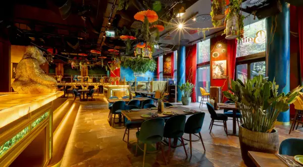 Złota małpa wita w jednej z klimatycznych restauracji Warszawa. Wnętrze pełne zieleni, czerwonych zasłon i egzotycznych dekoracji.