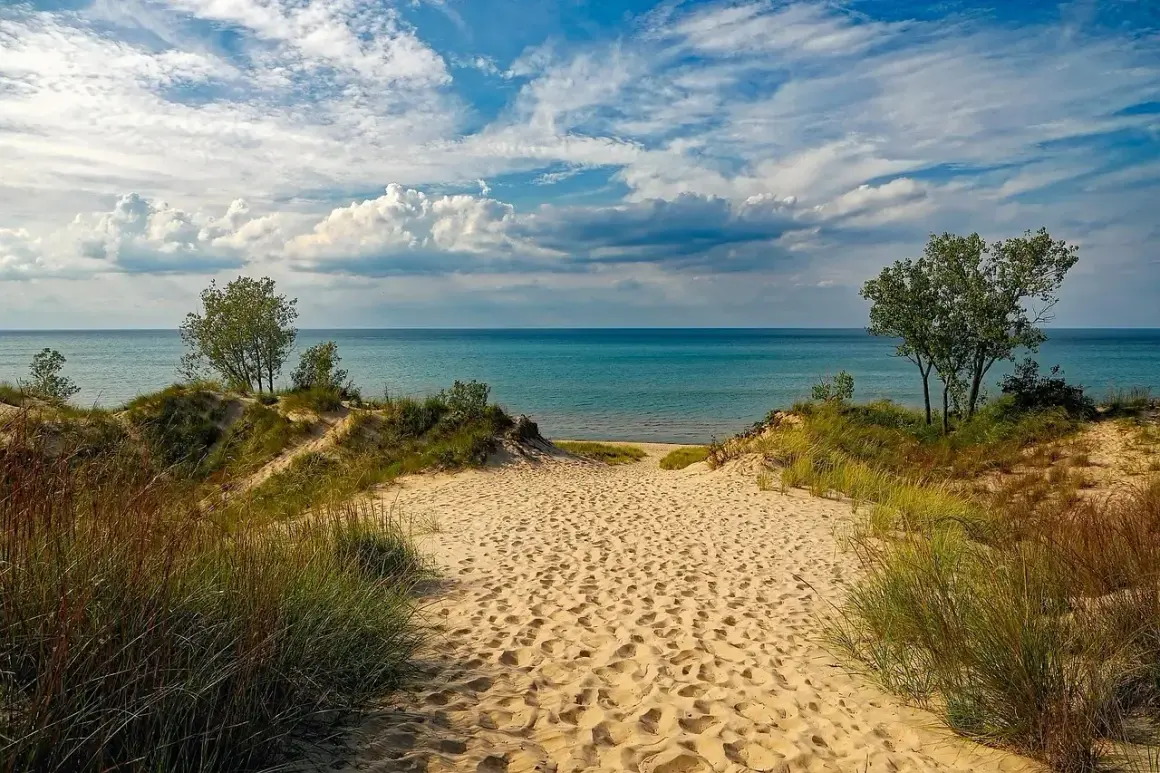 Ścieżka przez piaszczyste wydmy prowadzi do turkusowego jeziora. To idealne miejsce na relaks, jak na plaży nad Jeziorem Rożnowskim.