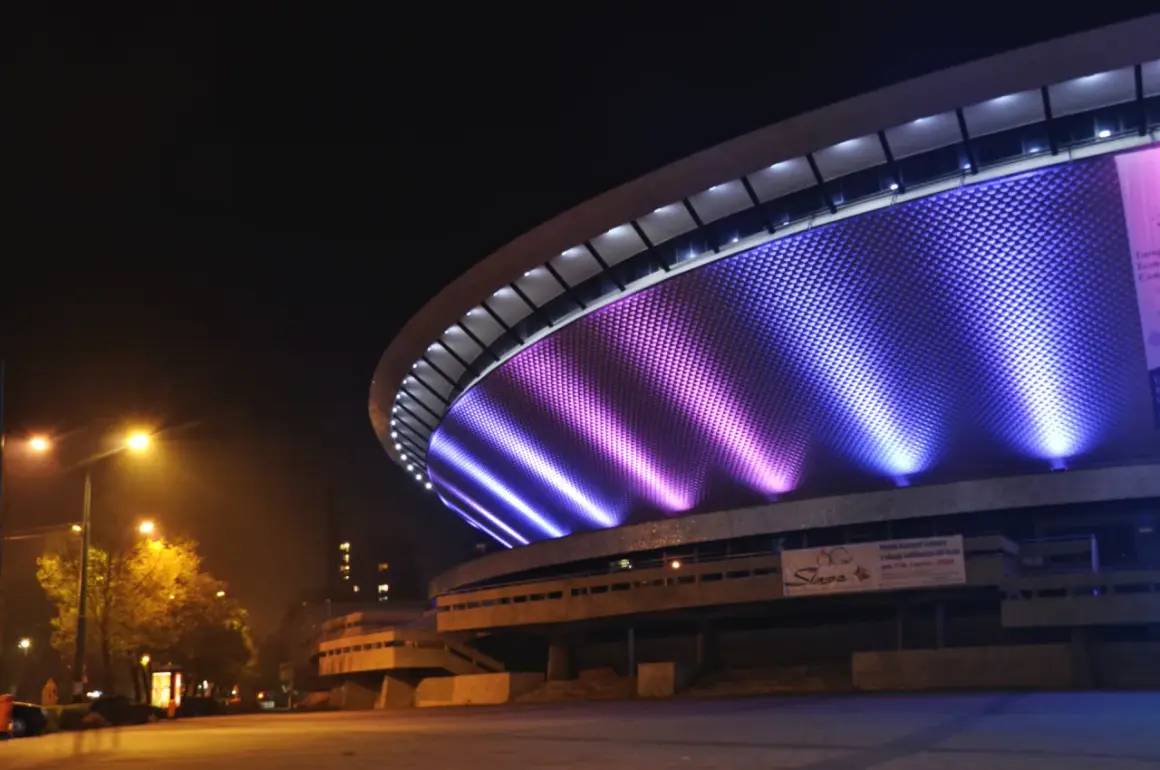 Nocne atrakcje w: Katowice. Spodek rozświetlony fioletowo-niebieskim światłem, nocą.