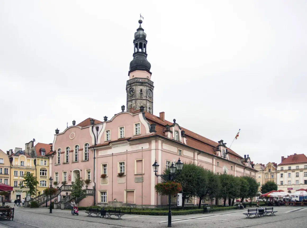 Różowy ratusz z wieżą zegarową to główna z bolesławiec atrakcje. Na rynku widać też kamienice i kawiarniane stoliki.
