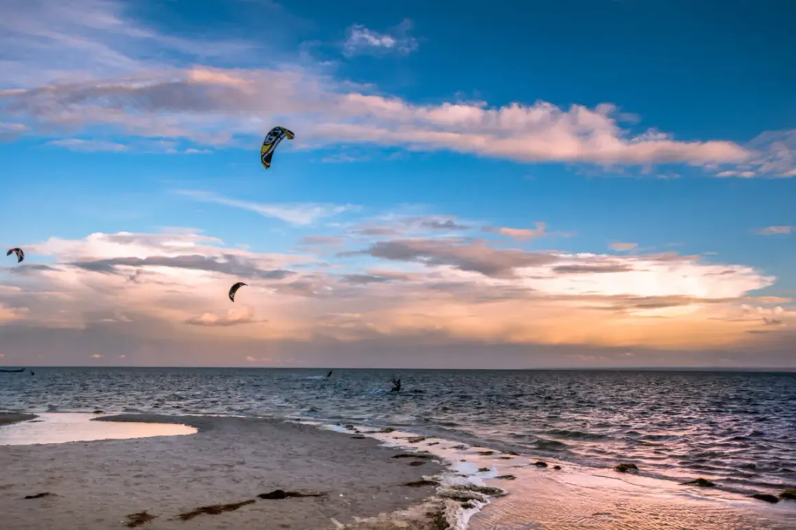Zachód słońca nad Bałtykiem. Kilku śmiałków uprawia kitesurfing w Polsce, unosząc się na falach pod kolorowym niebem.