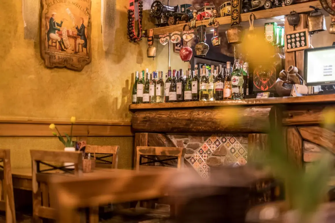 Drewniane stoły i krzesła w przytulnych restauracjach w Szklarskiej Porębie. Na półce rząd butelek wina, a nad nimi ozdoby.