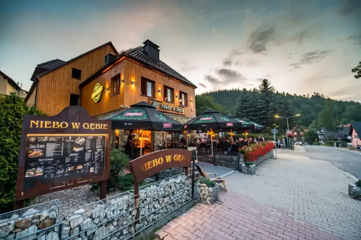 Restauracja "Niebo w Gębie" w Karpaczu oferuje pyszne jedzenie. Widać tu menu i stoliki na zewnątrz.