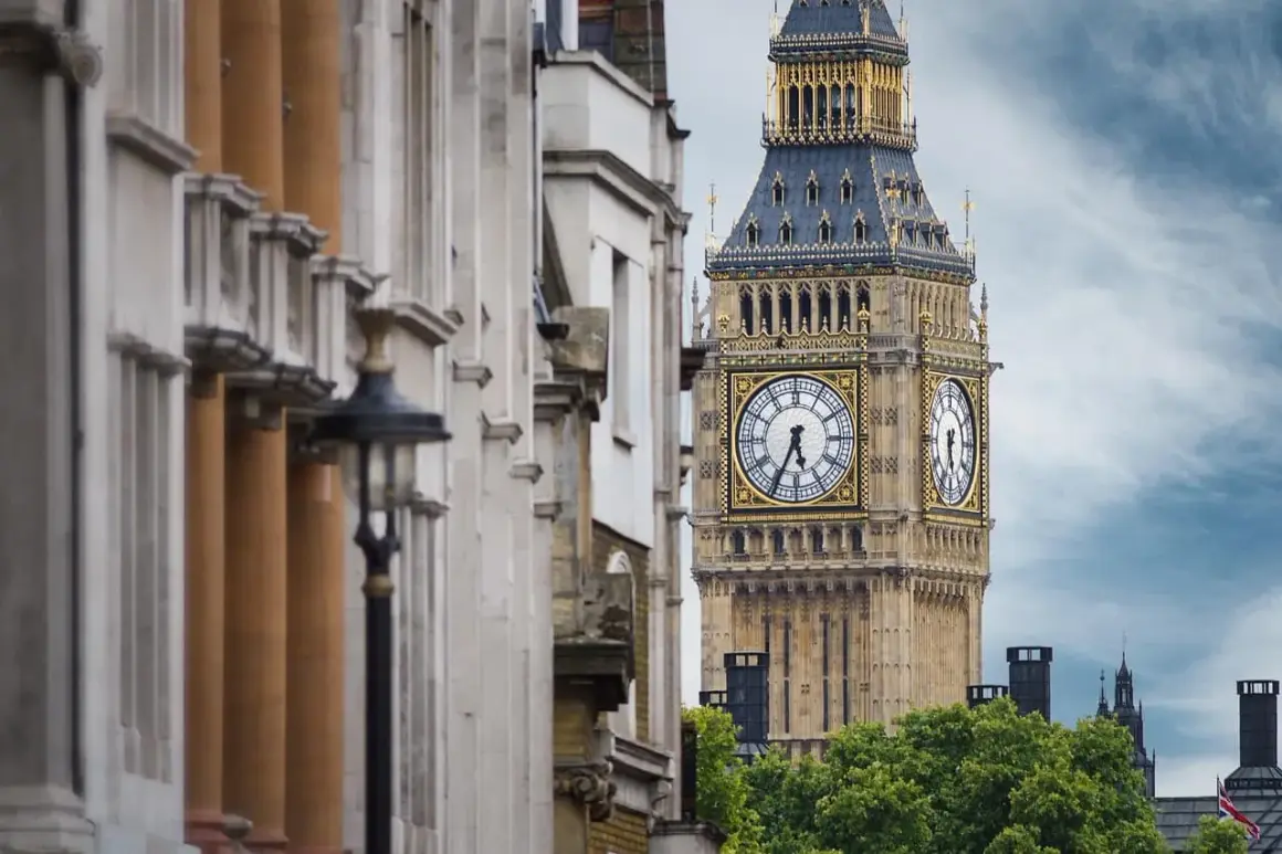 Big Ben, jedna z głównych atrakcji Anglii, góruje nad zielonymi drzewami. Obok widać zabytkową architekturę.