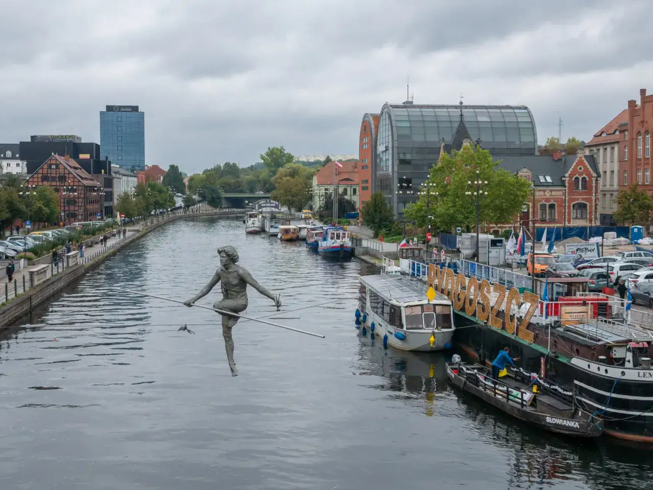 Nietypowe atrakcje Bydgoszcz: rzeźba na linie nad Brdą, statki i budynki nad rzeką.