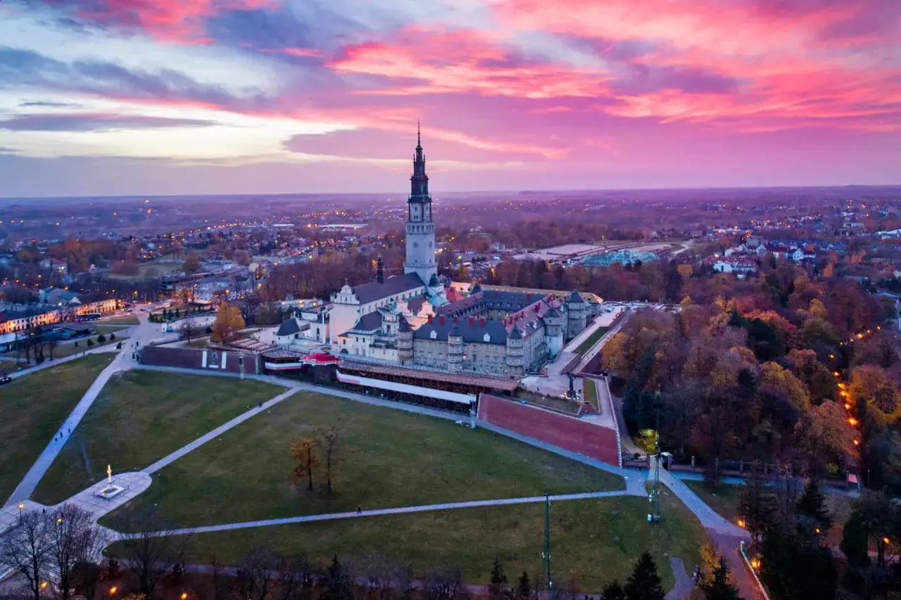 Jasny zachód słońca nad Jasną Górą, jedną z głównych częstochowskich atrakcji. Monumentalny klasztor z wieżą góruje nad miastem.