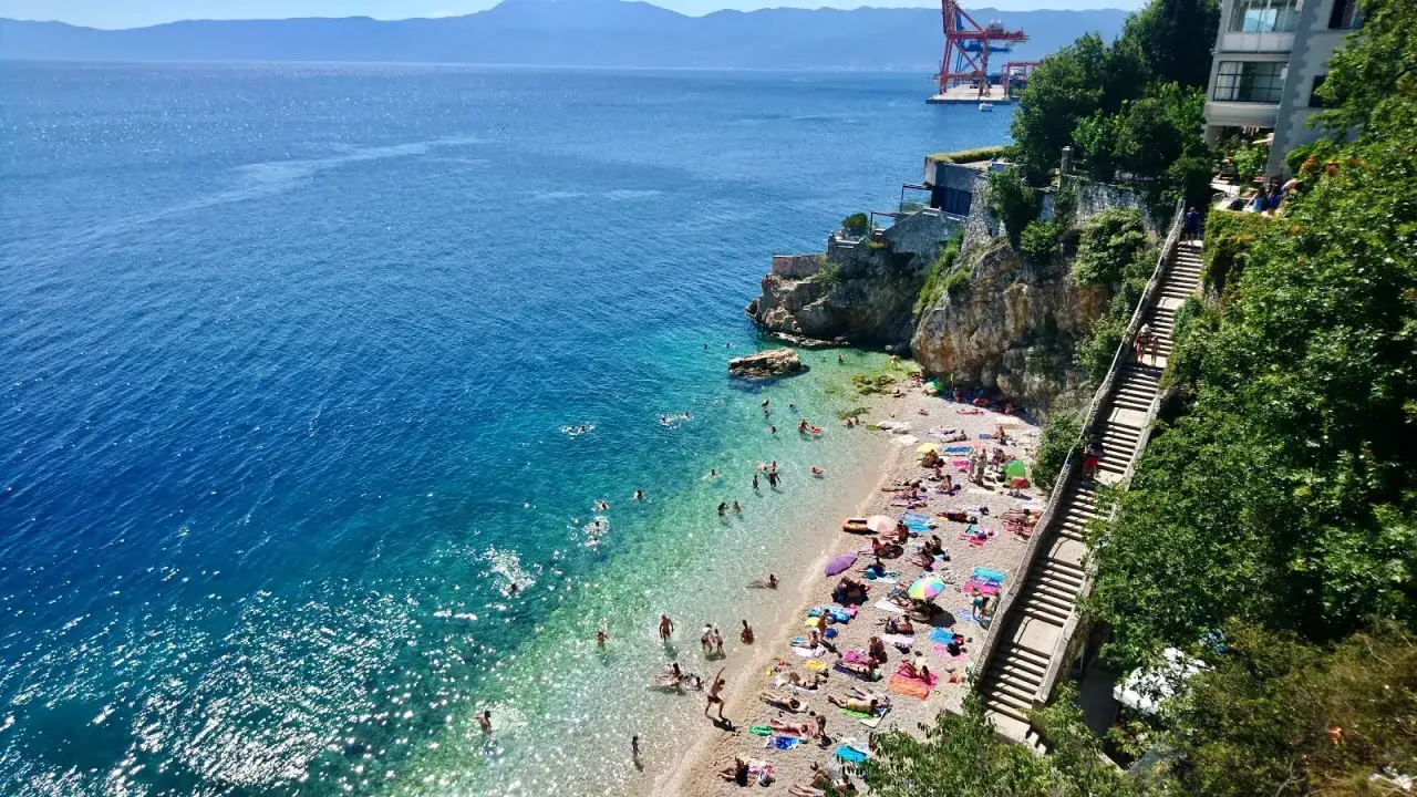 Słoneczne rijeka plaże pełne ludzi kąpiących się w krystalicznie czystej wodzie i opalających się na kamieniach.