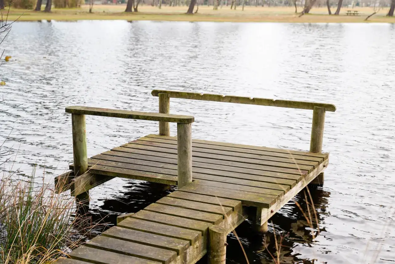 Drewniany pomost na spokojnej plaży nad jeziorem, otoczony trawami. Idealne miejsce na relaks i podziwianie widok&oacute;w.