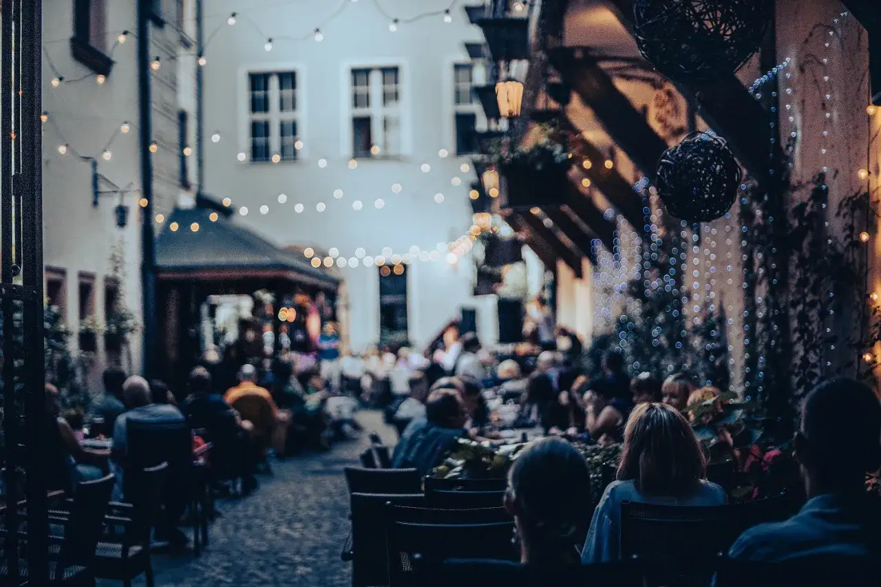 Wieczorny gwar wrocławskich restauracji na Rynku. Ludzie siedzą przy stolikach, delektując się atmosferą i światłem lampek.