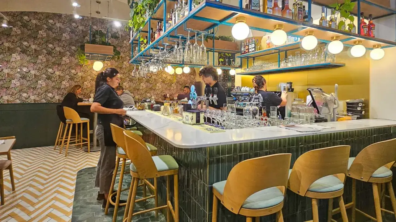 Wnętrze lokalu z barem, gdzie pracownicy przygotowują napoje. W tle widać gości. Idealne miejsce z polecane restauracje poznań.