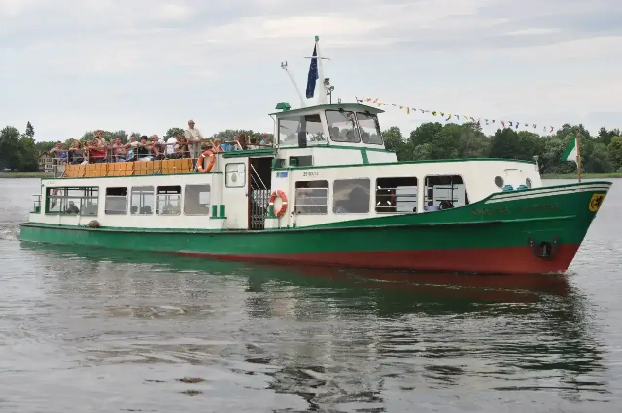 Zielony statek z pasażerami na pokładzie, pływający po jeziorze. Jedna z atrakcji Szczecinka.