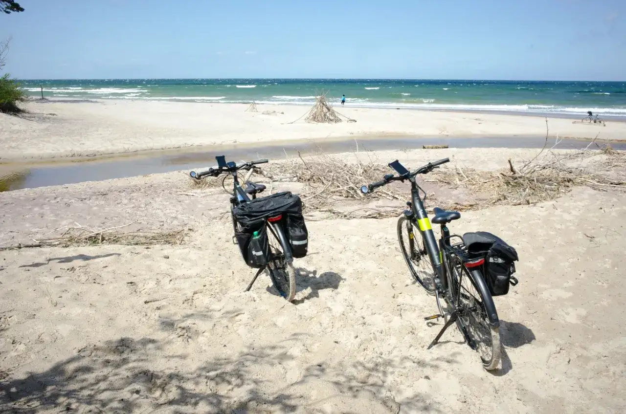 Dwa rowery z sakwami na piaszczystej plaży, gotowe na odkrywanie tras rowerowych nad morzem.