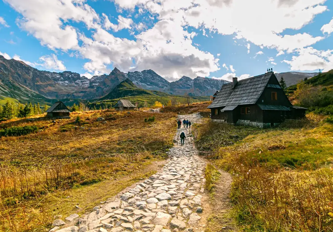 Kamienista ścieżka prowadzi przez Rusinową Polanę do drewnianych bacówek. W tle majestatyczne Tatry.