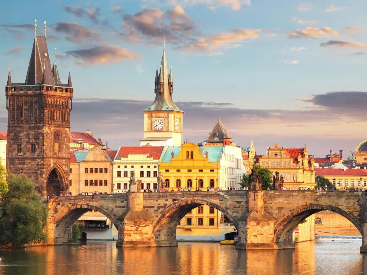 Praga co zobaczyć w jeden dzień: Most Karola z wieżami i kolorowymi kamienicami o zachodzie słońca.