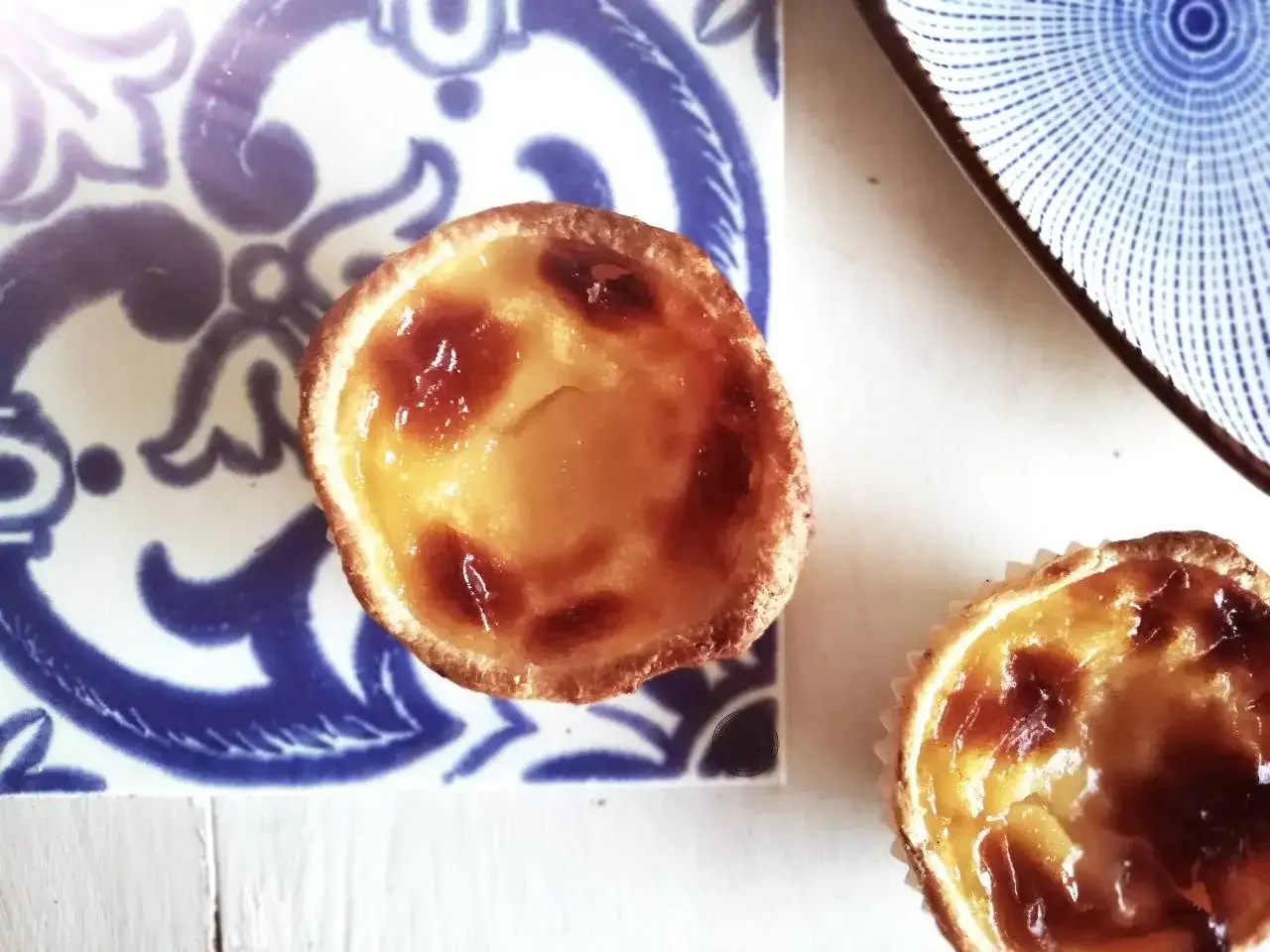 Dwa pyszne pastel de nata, klasyk kuchni portugalskiej, na niebiesko-białej płytce.