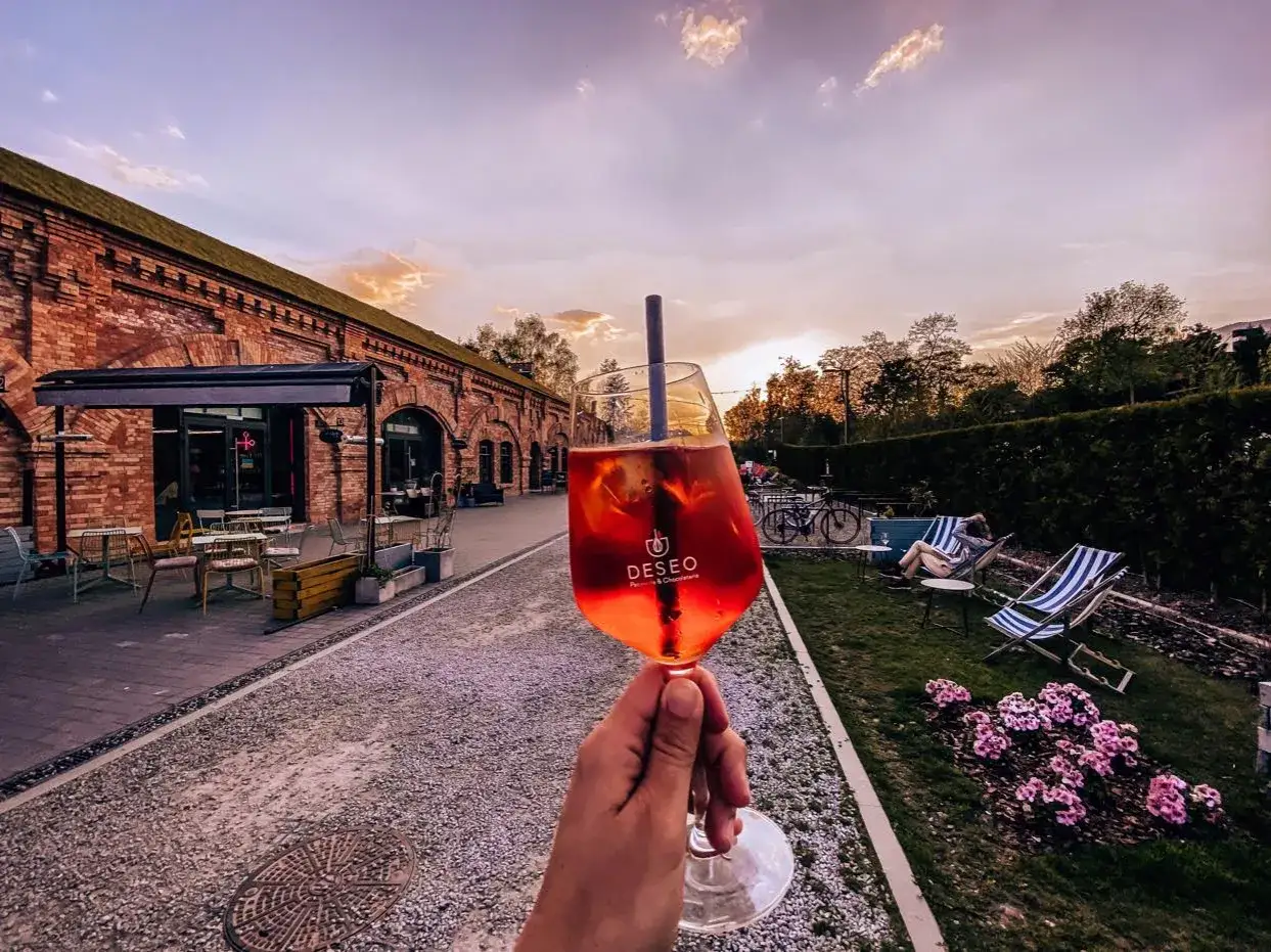 Orzeźwiający drink w jednej z klimatycznych restauracji Warszawa. Zach&oacute;d słońca nad ceglanymi budynkami i zielonym ogrodem.