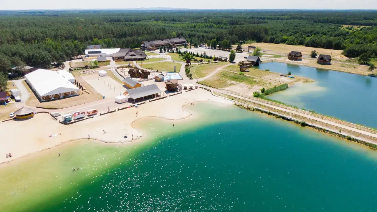 Malownicze jeziora opolskie z piaszczystą plażą, turkusową wodą i kompleksem wypoczynkowym w otoczeniu lasu.