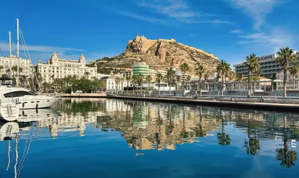 Widok na port i zamek Santa Barbara w Alicante. Luksusowe jachty odbijają się w spokojnej wodzie.