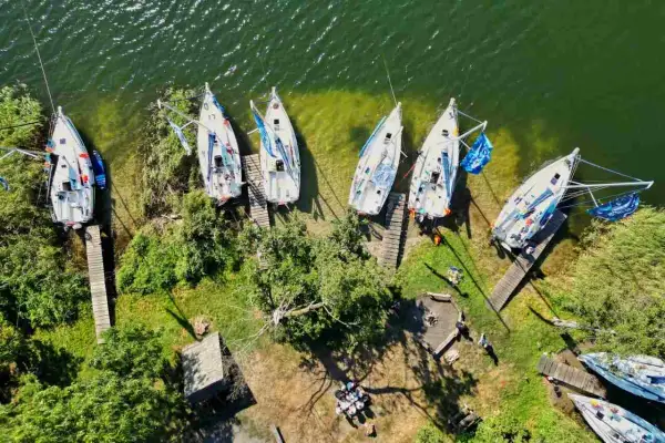 Mazury atrakcje wodne: białe żaglówki cumują przy brzegu, zielona trawa i drzewa tworzą malowniczy krajobraz.