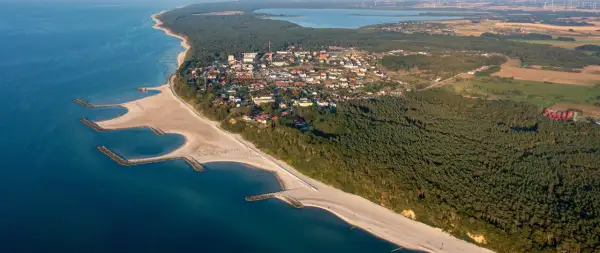 Jarosławiec: widok z lotu ptaka na plażę z falochronami, las i zabudowania.
