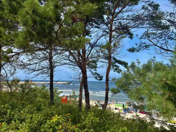 Widok na plażę w Mrzeżynie, z ludźmi odpoczywającymi na piasku i morzem w tle. To jedne z wielu mrzeżyno atrakcje.