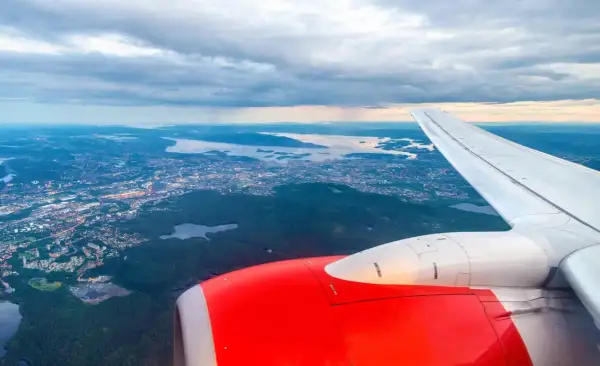 Widok z samolotu na Oslo Torp i okoliczne fiordy. Czerwony silnik i białe skrzydło samolotu na pierwszym planie.
